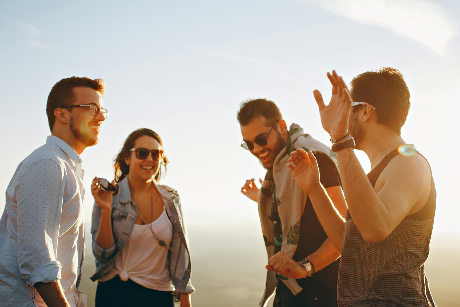 Vorteile von Freundschaften in einer digitalisierten Welt - Drei Männer und eine Frau lachen bei strahlendem Sonnenschein